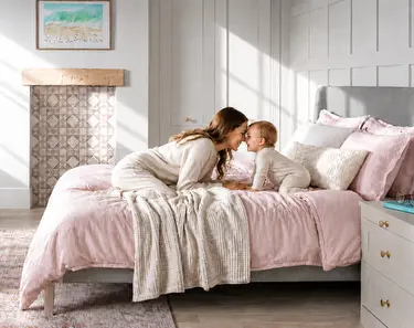 A mother and child in a bedroom with a pink duvet
