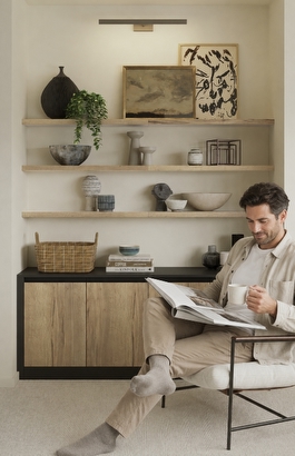 A man sat reading in a room with shelves and storage space
